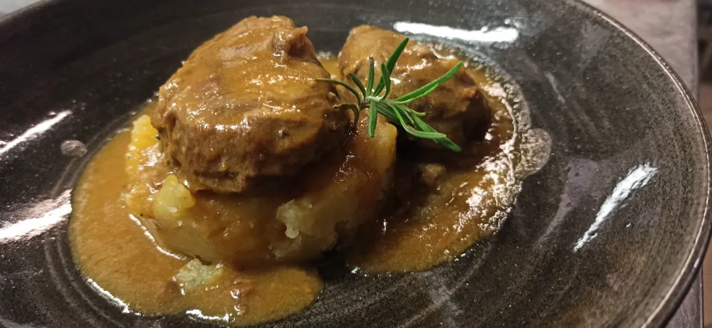 Slow-cooked pork cheek (ganassino) braised in beer with crushed potatoes, a tender traditional specialty at Osteria d'Asti, Arona.